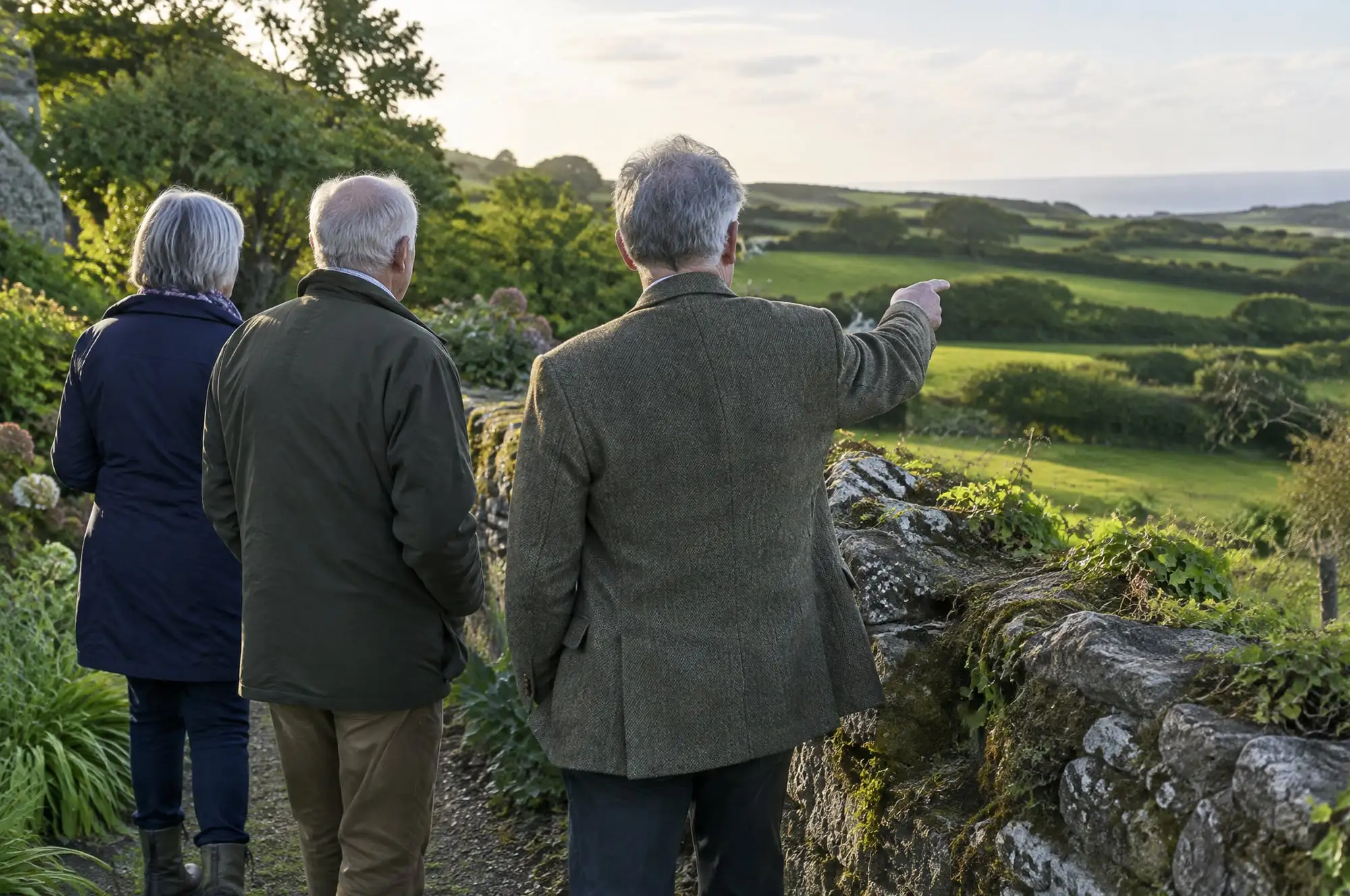 An agent in a tweed jacket walking a stone boundary wall with a couple, pointing across the fields